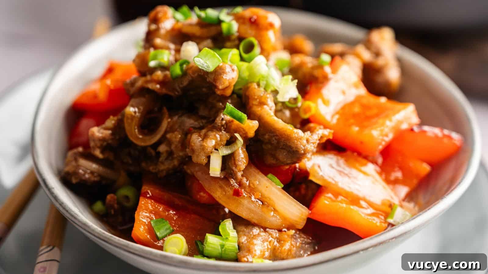 A bowl of stir-fried beef with red bell peppers, onions, and chopped green onions, served on a white plate.