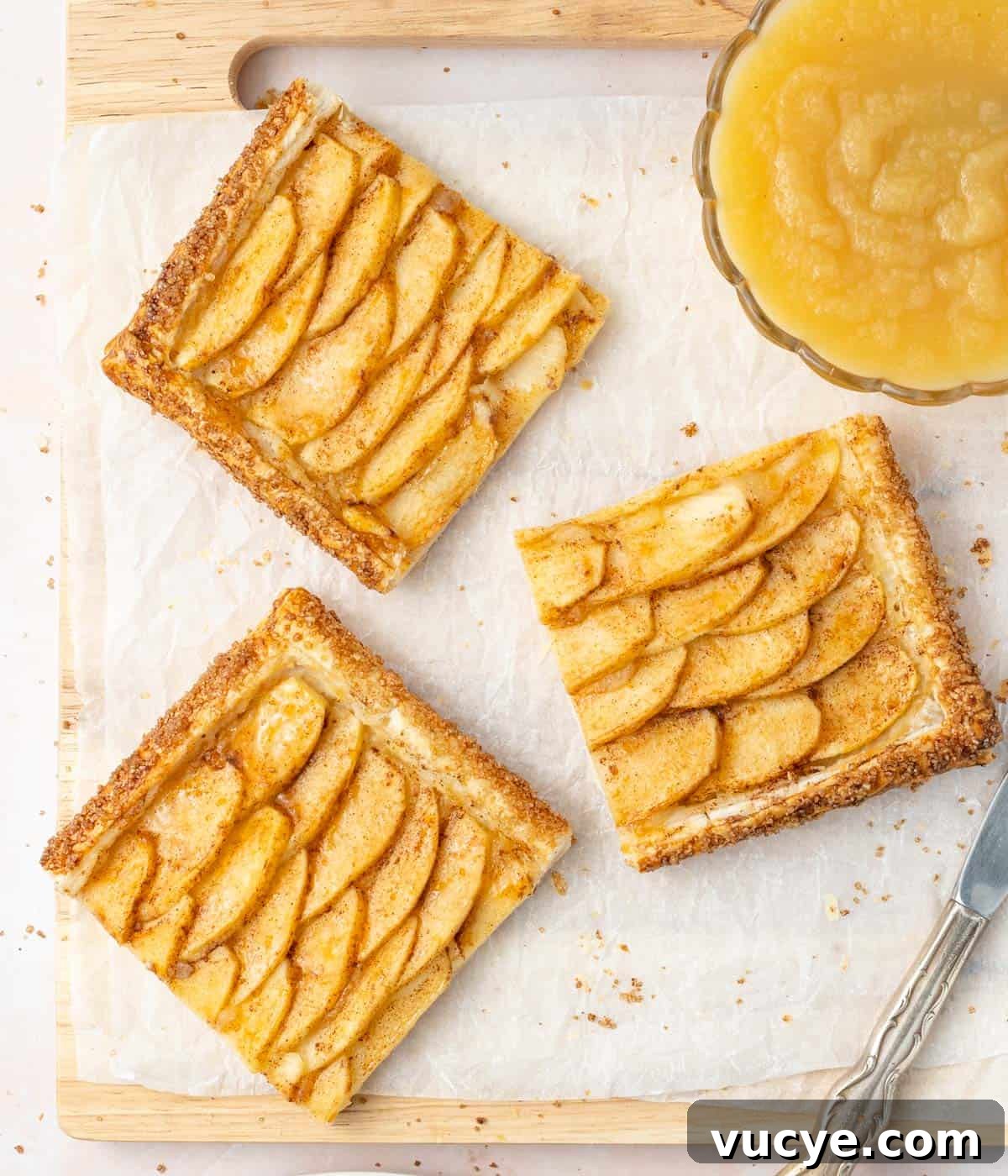 3 slices of tart on a cutting board with a bowl filled with applesauce.