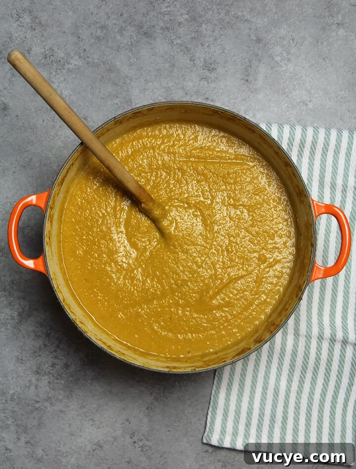 A finished pot of butternut squash soup with a wooden spoon in it.