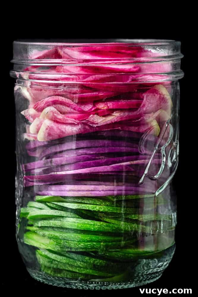 Crunchy Tangy Pickled Radishes Ready in Minutes 3 A glass mason jar packed with thinly sliced green, purple and pink radishes, stacked by color, grey background.