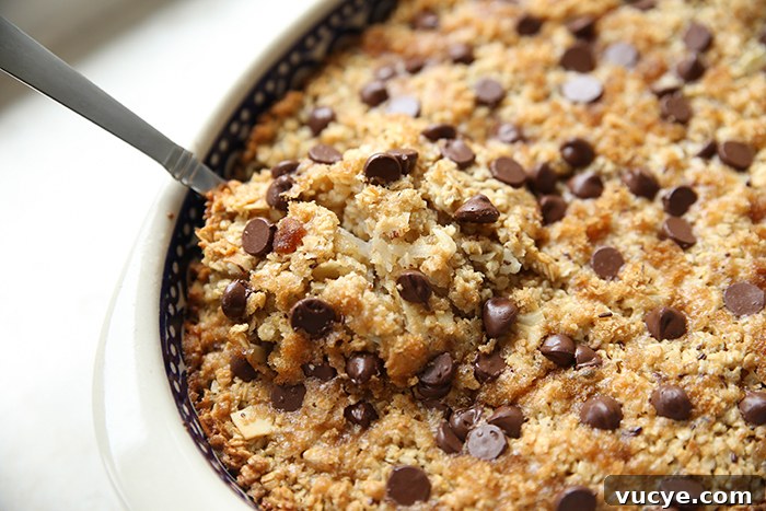 Almond Joy Baked Oatmeal Recipe – Coconut, Almond & Chocolate Breakfast 4 A partial picture of an oval bowl of almond joy oatmeal with a spoon inserted diagonally on the left.