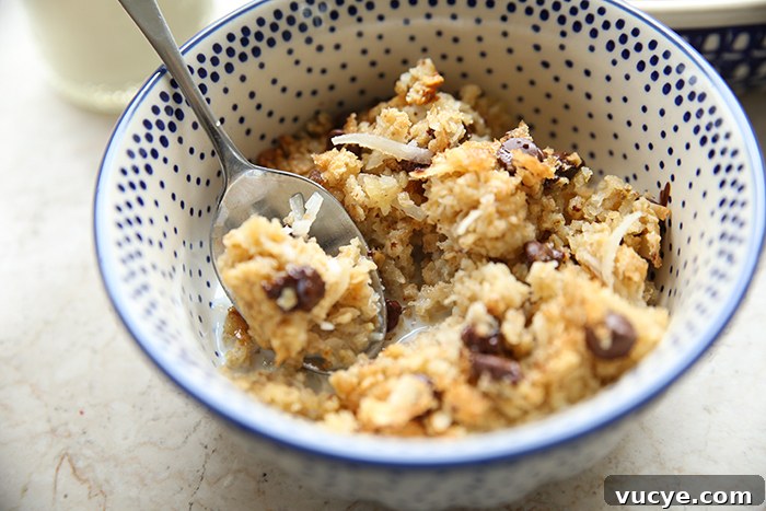 Almond Joy Baked Oatmeal Recipe – Coconut, Almond & Chocolate Breakfast 5 A serving of almond joy oatmeal with milk in a white and blue dotted bowl with a spoon handle vertically placed on the rim and the head of spoon with oatmeal resting on top of the almond joy oatmeal.