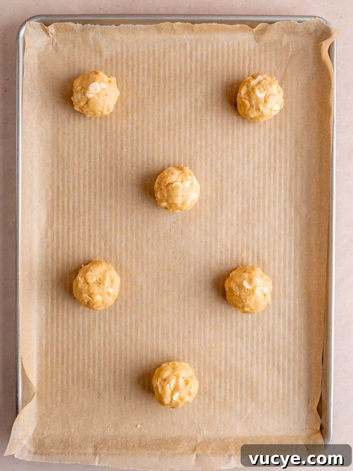 White Chocolate Macadamia Nut Cookies Recipe You’ll Love 7 Scoops of white chocolate macadamia cookie dough on a baking sheet.