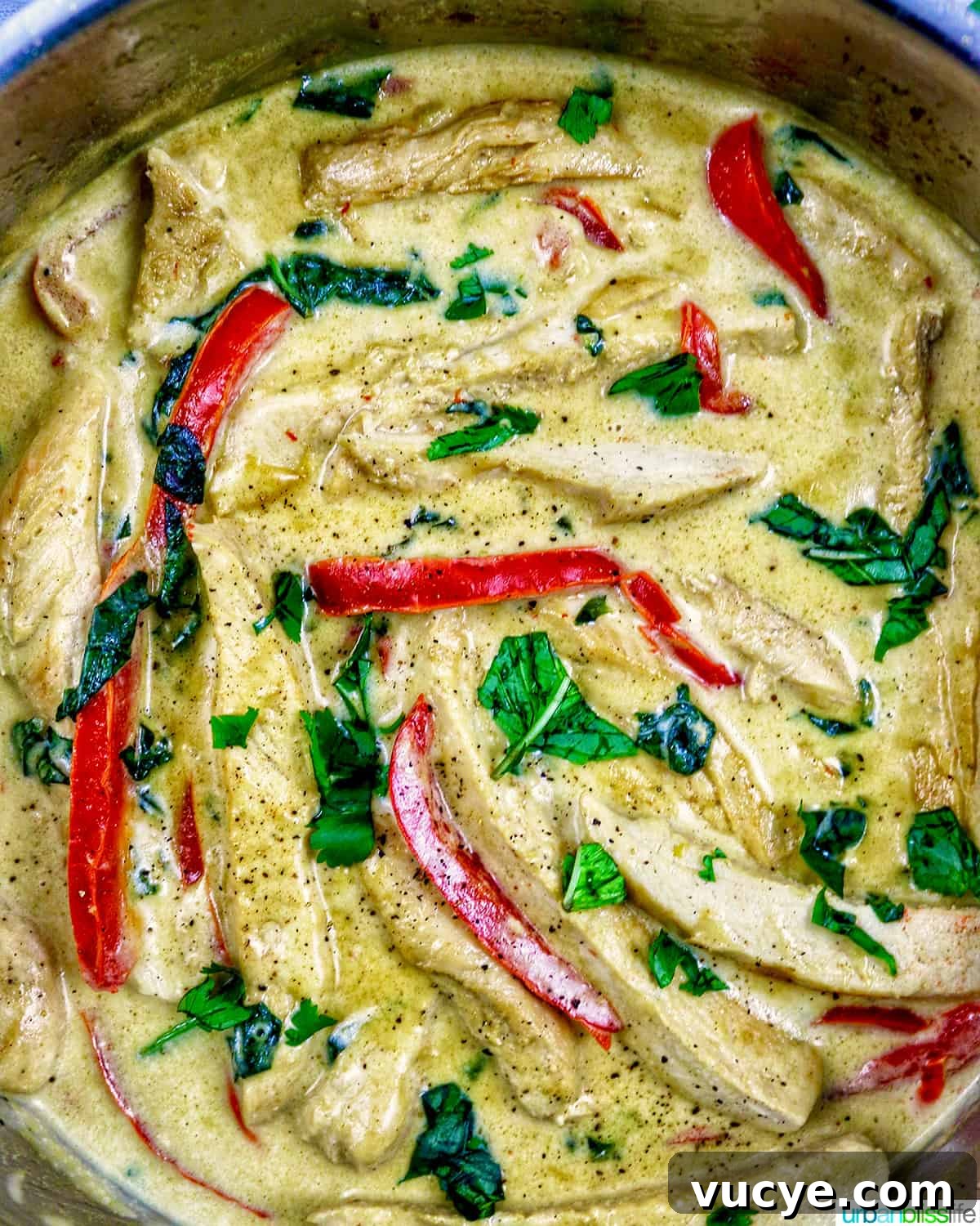 chicken, red bell peppers, cilantro simmering in coconut milk cream sauce in a pan.