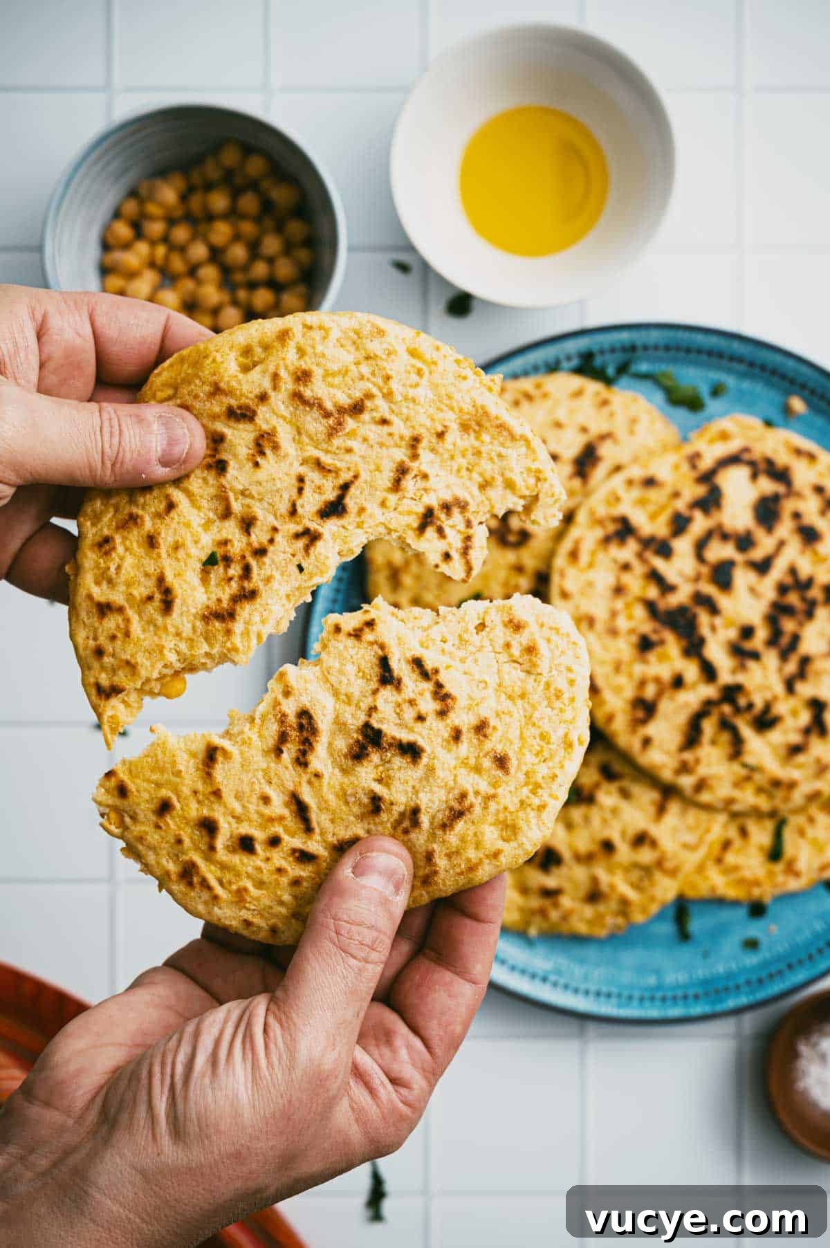 Hands tearing soft chickpea flatbread in half.