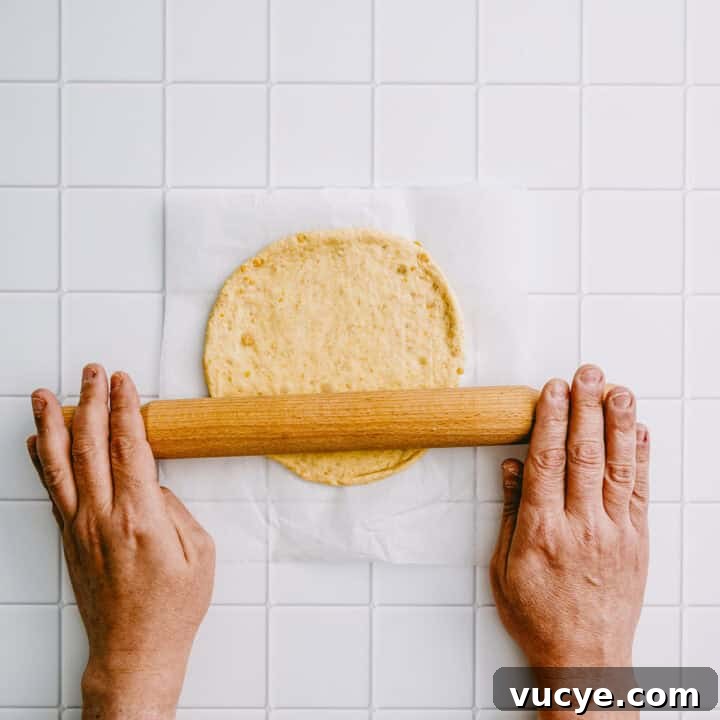Hands rolling out chickpea flatbread dough with a rolling pin.