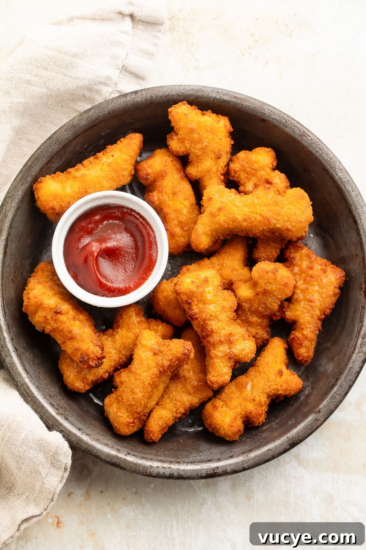 Air fryer dino nuggets on a plate with a small ramekin of ketchup.