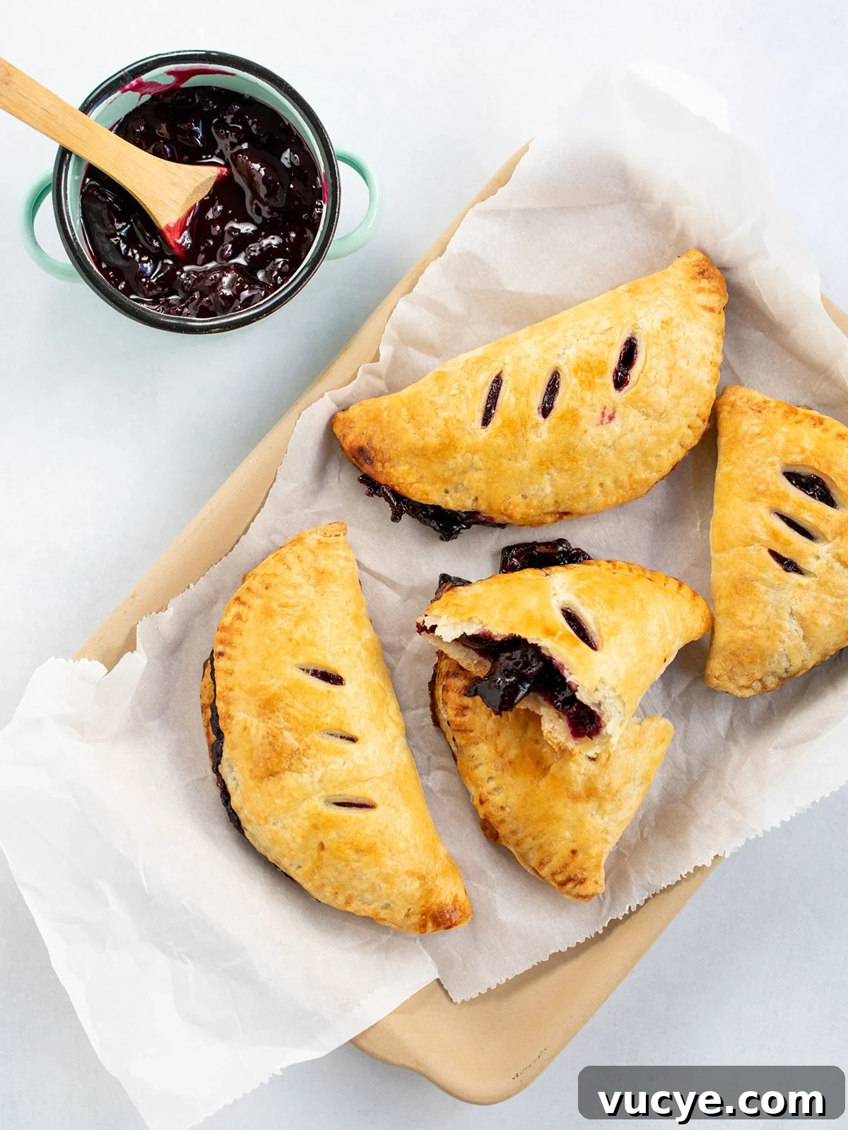 Mini Cherry Hand Pies: Bite-Sized Fruit Pastries Recipe 2 Top down view of mini cherry pies on parchment with extra pie filling on the side.