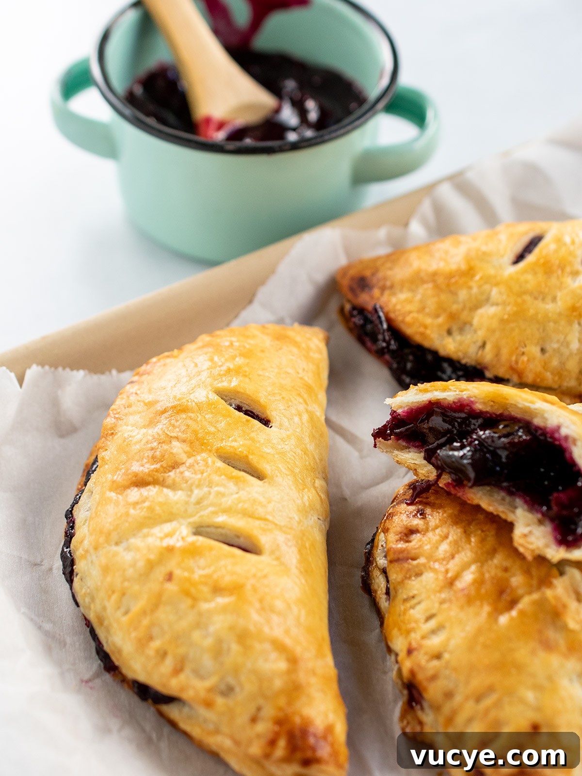 Mini Cherry Hand Pies: Bite-Sized Fruit Pastries Recipe 11 Close up view of baked pie dough hand pie with extra pie filling in the background.