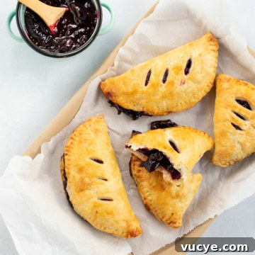 Mini Cherry Hand Pies: Bite-Sized Fruit Pastries Recipe 13 Top down view of mini cherry pies on parchment with extra pie filling on the side.