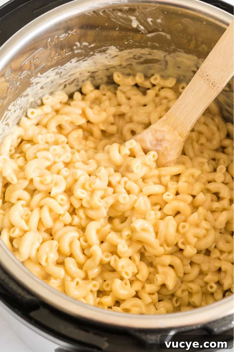 Macaroni and cheese is total comfort food! This easy Instant Pot Mac and Cheese recipe is ready in 30 mins for a dinner your family will love! macaroni and cheese in an instant pot with a wooden spoon