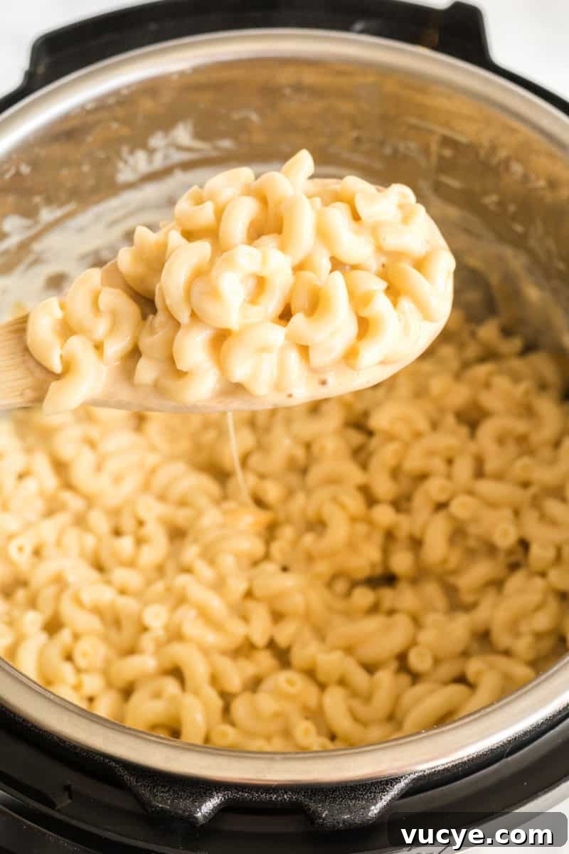 Macaroni and cheese is total comfort food! This easy Instant Pot Mac and Cheese recipe is ready in 30 mins for a dinner your family will love! spoonful of mac and cheese over an instant pot with sauce dripping from the spoon