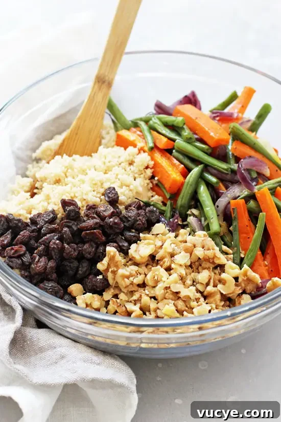 Vegan couscous salad with roasted vegetables! Packed with whole wheat couscous, green beans, carrots, walnuts and raisins, it makes for a perfect healthy & quick meal or side! Finished with a simple maple orange dressing! A large glass bowl filled with couscous, roasted veggies, walnuts and raisins.