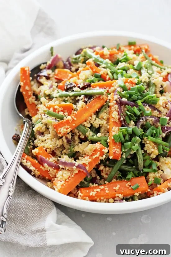 Healthy and easy vegan couscous salad! Filled with roasted veggies, walnuts, raisins and a dreamy maple tahini orange dressing. Light yet filling, it’s excellent for lunch or dinner! A white bowl filled with Vegan Couscous Salad and a silver spoon on the side.