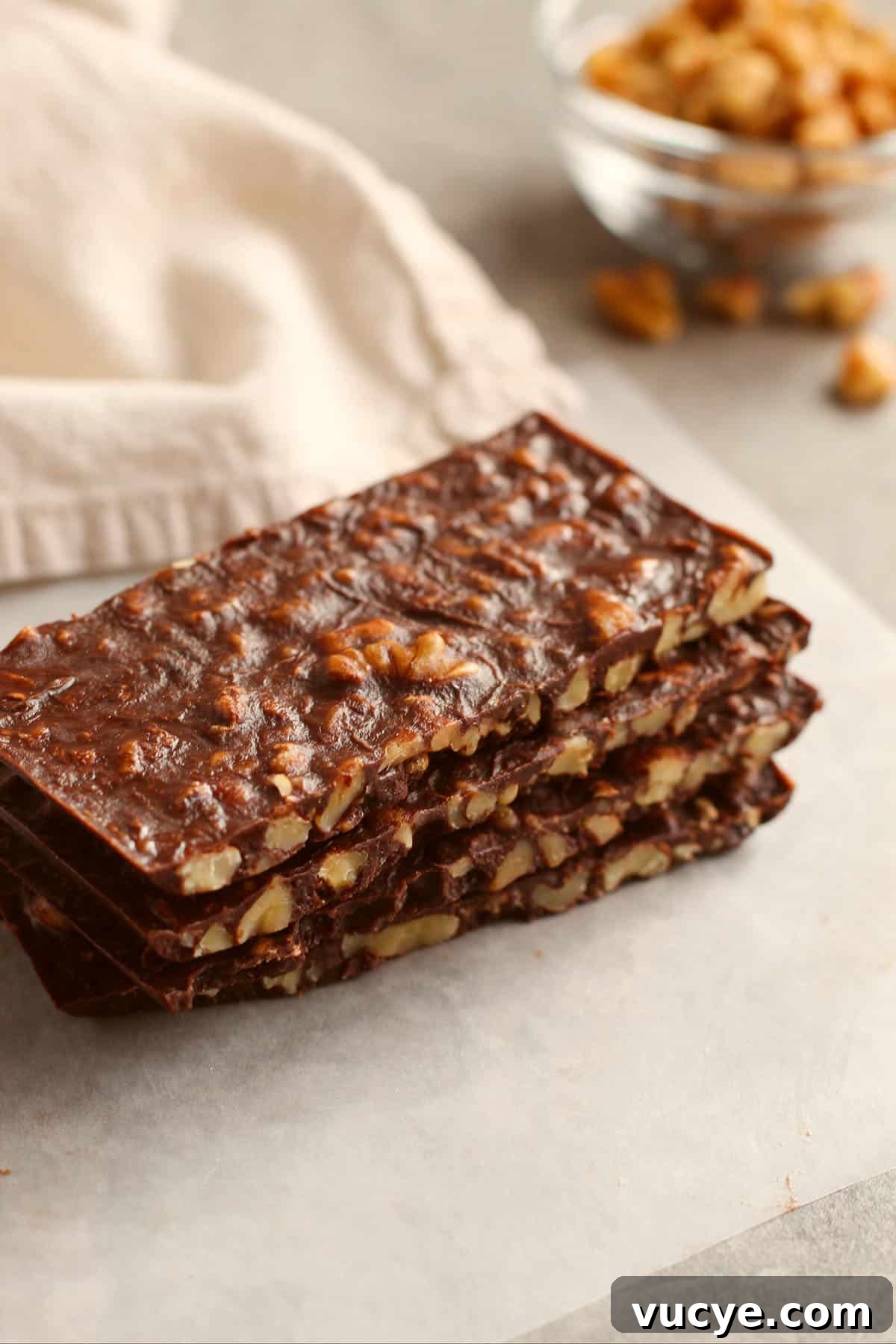 Keto Chocolate Crunch Bars Recipe — Low-Carb Chocolate Snack 2 rectangular shaped sliced bars stacked on top of each other with beige napkin and walnut pieces in background