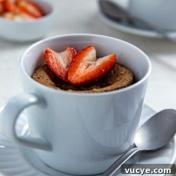 Cooked mug cake in white dish with sliced strawberry on top.