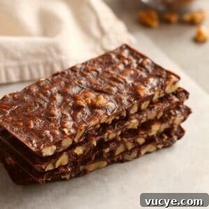 Keto Chocolate Crunch Bars Recipe — Low-Carb Chocolate Snack 10 rectangular shaped sliced bars stacked on top of each other with beige napkin and walnut pieces in background