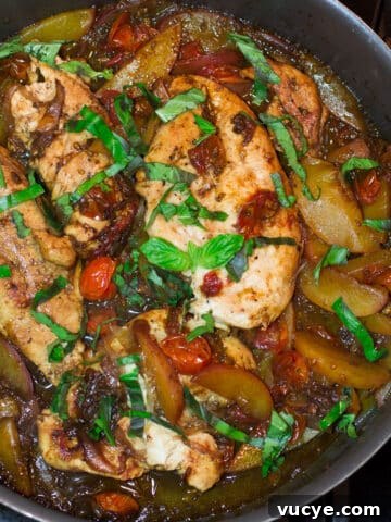 Skillet containing chicken, peaches, tomato topped with basil in a balsamic vinegar glaze.