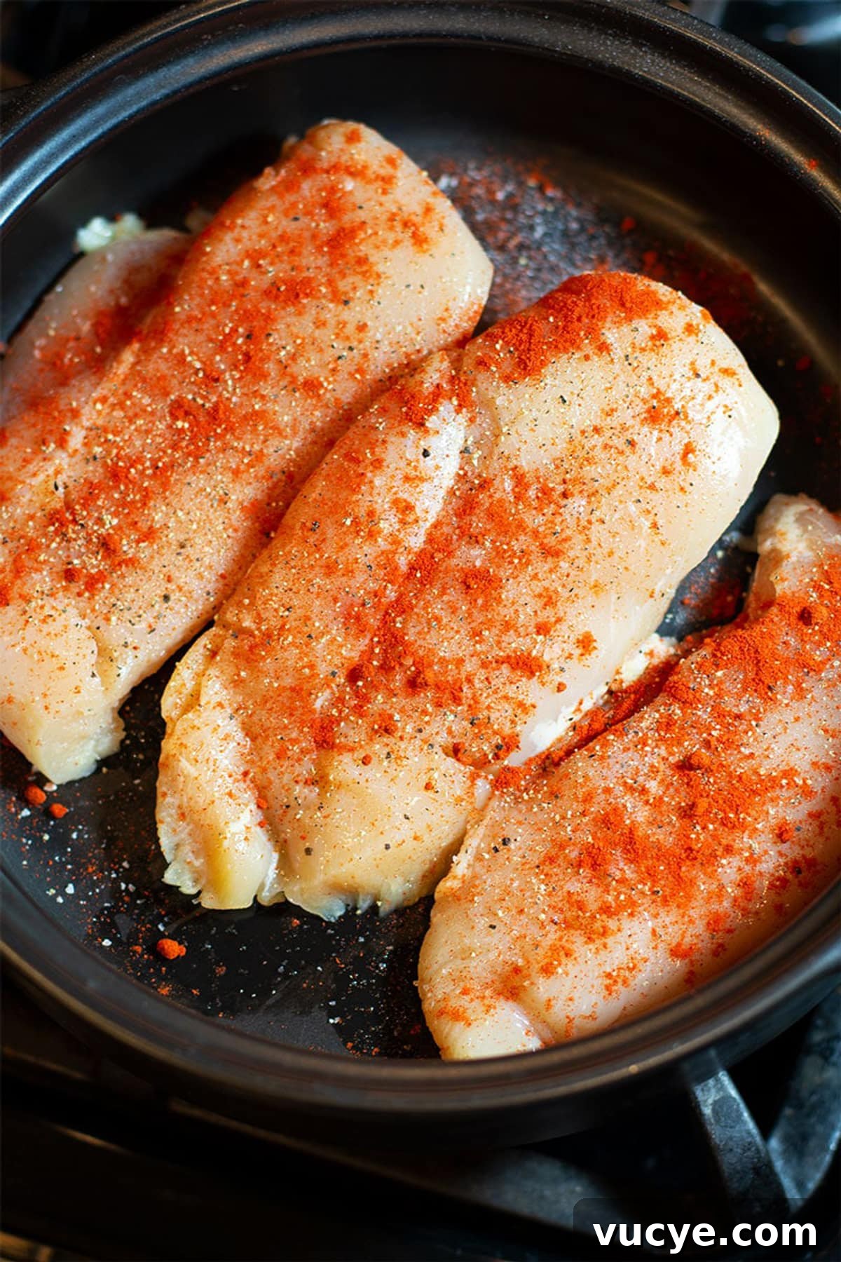 Three chicken breasts sprinkled with smoked Paprika, salt and pepper in a black pan.
