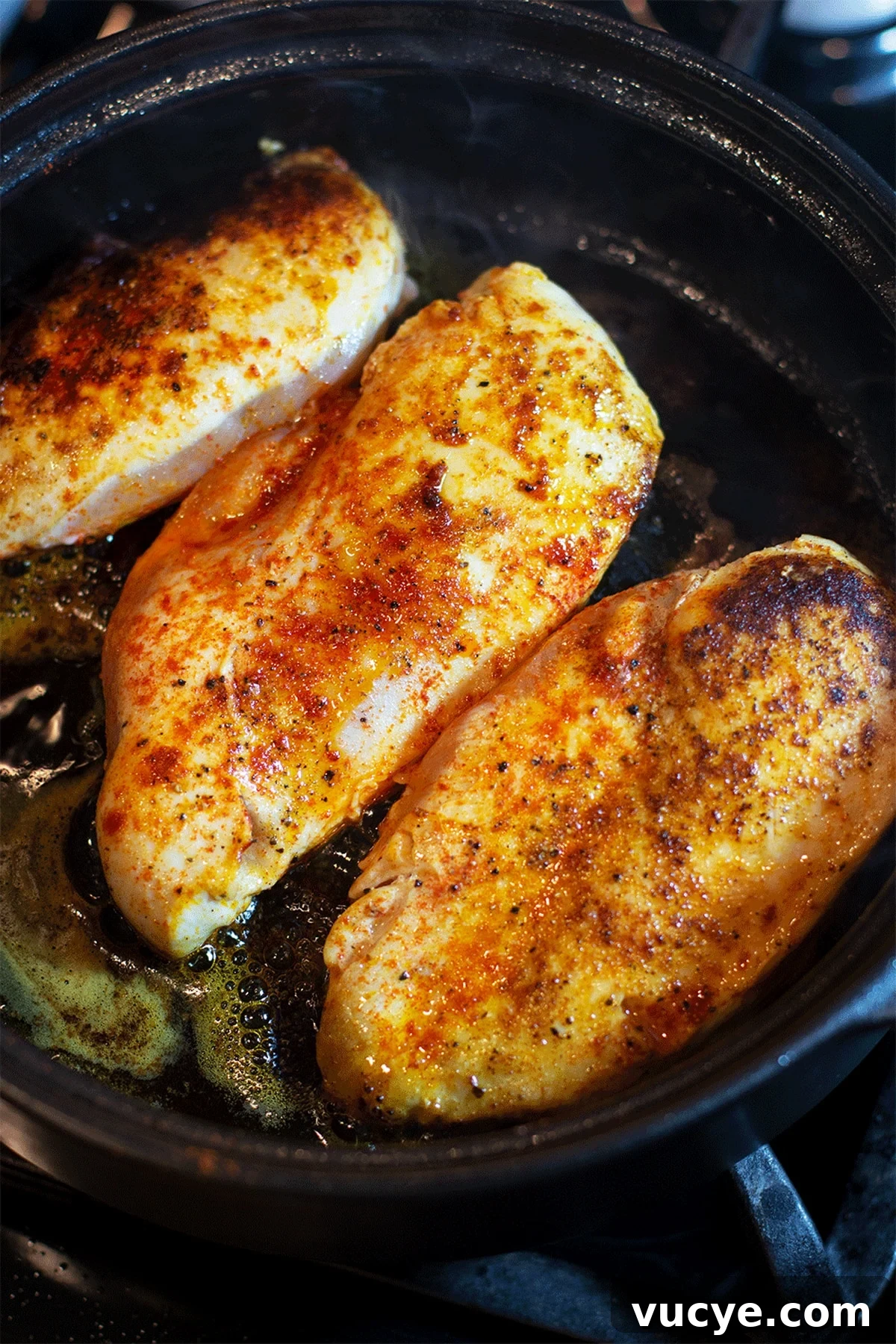 Three sauteed chicken breasts in a black pan.