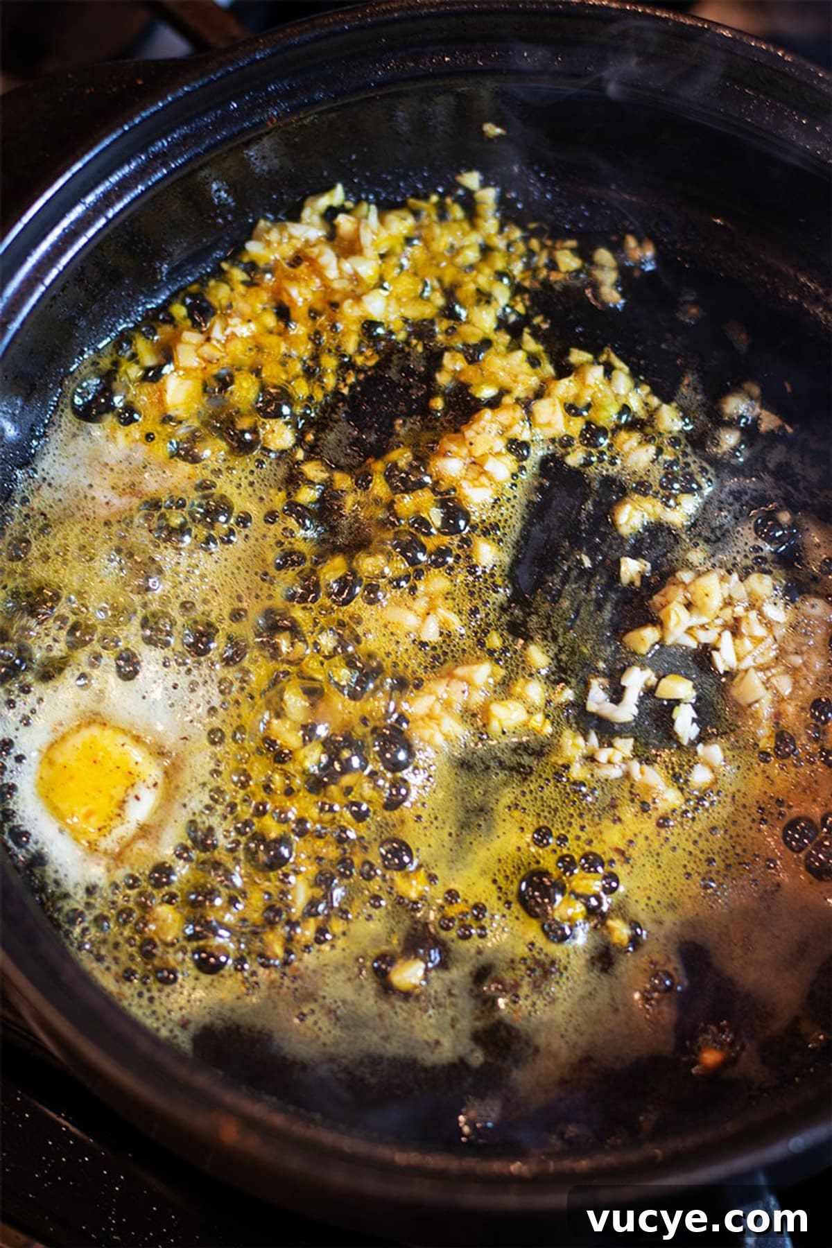 Chopped garlic and butter sauteing in a black pan.
