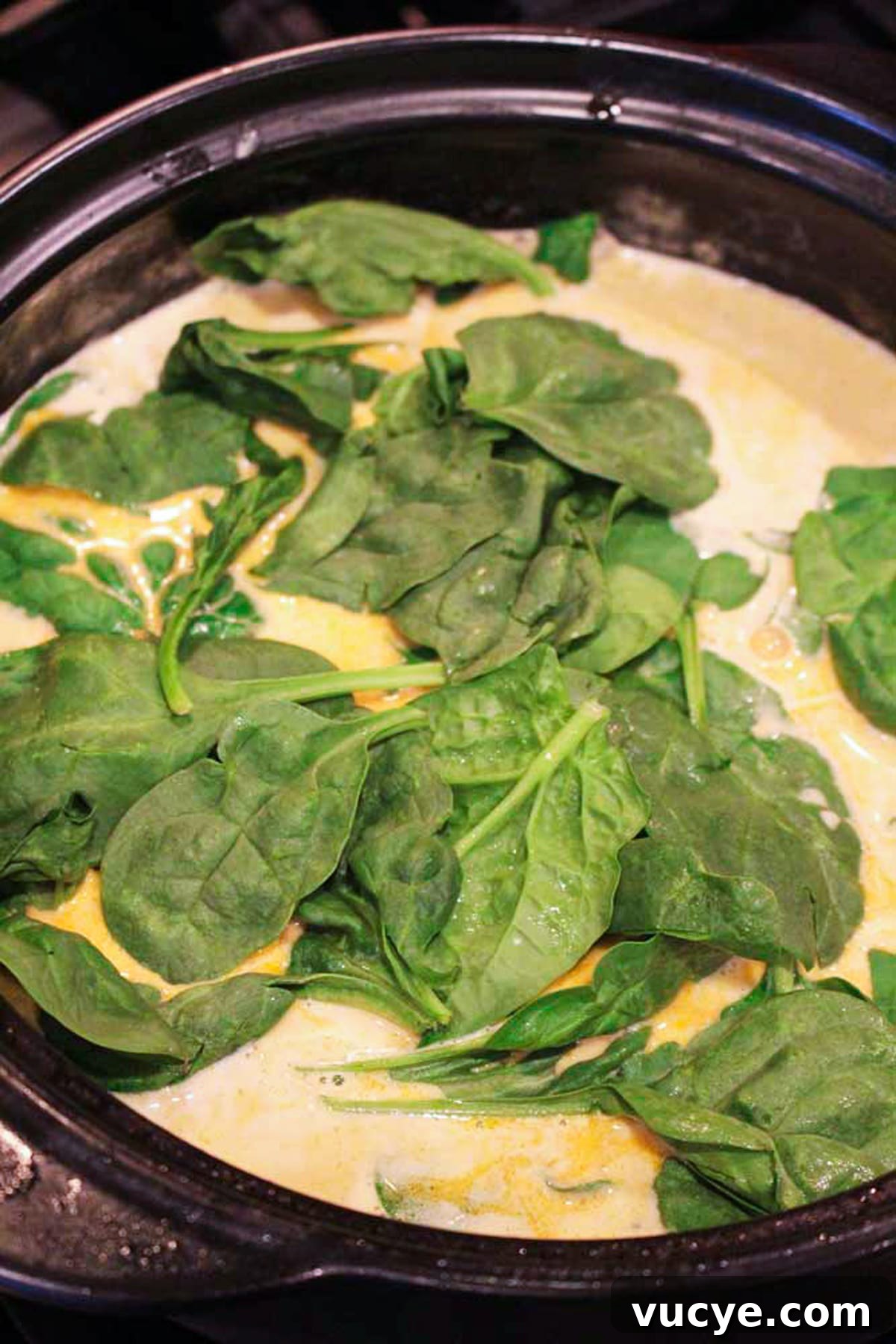 Black pan containing lemon butter cream sauce with fresh spinach.