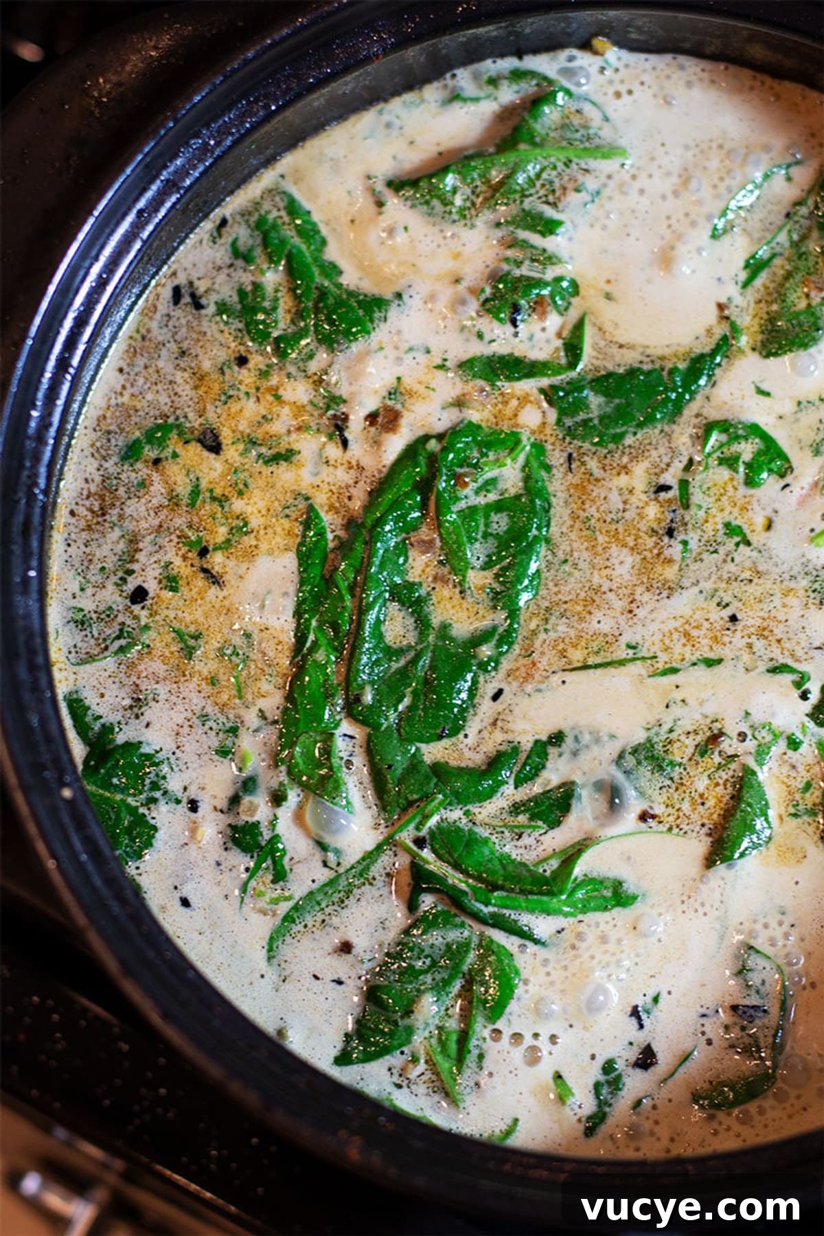 Lemon Butter Cream sauce with spinach sauteing in a black pan.