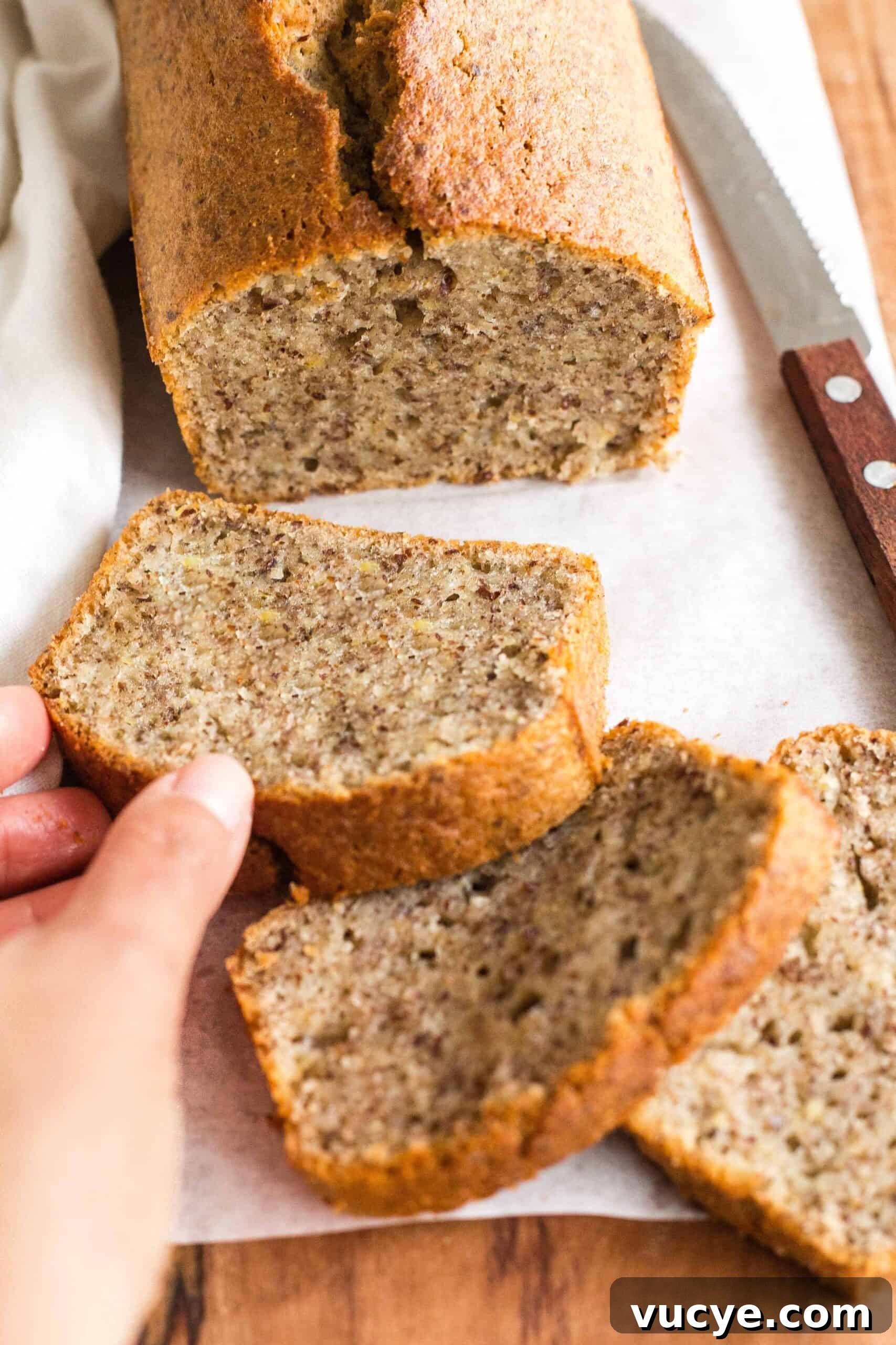 Easy Flaxseed Bread (Gluten-Free, Dairy-Free) Reaching for a slice of flax bread from a wooden board.
