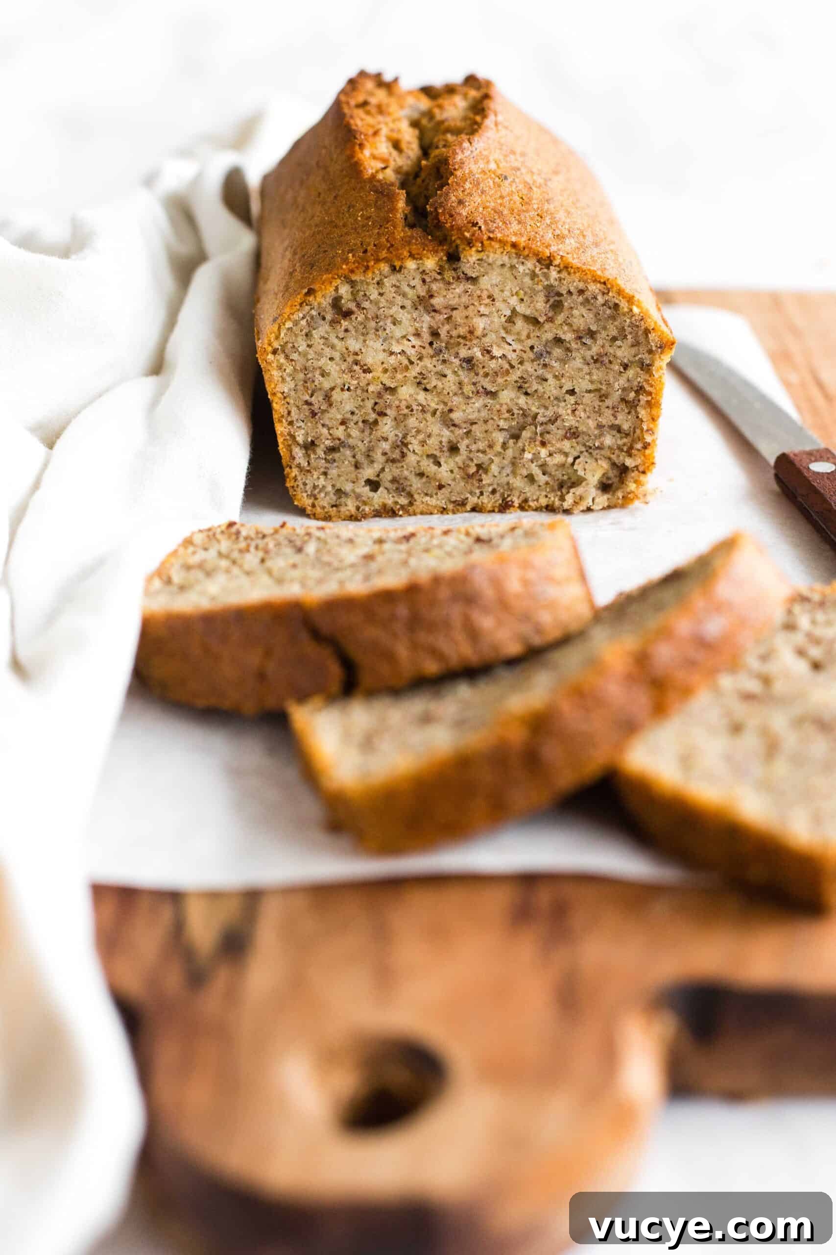 Easy Flaxseed Bread (Gluten-Free, Dairy-Free) A half-sliced loaf of flax bread on a parchment-lined wooden board.
