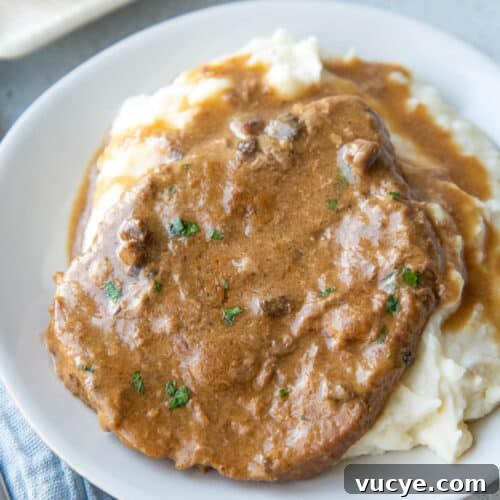 cube steak with gravy on a bed of mashed potatoes on a white plate.