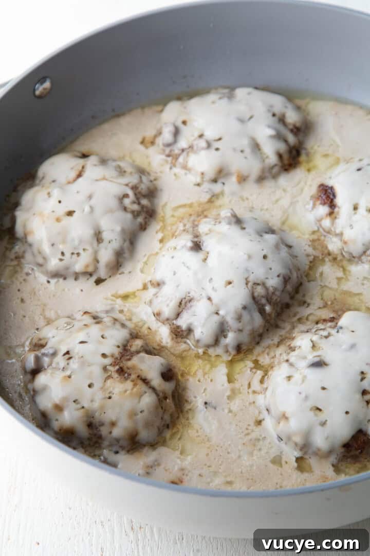 cooked beef patties covered with cream of mushroom soup in a skillet.