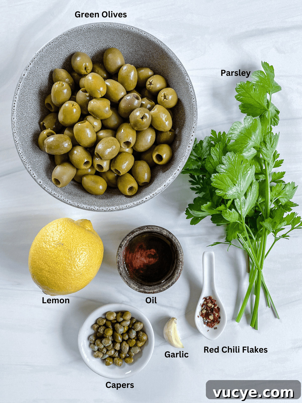 Ingredients for Green Olive Tapenade measured out on a white surface.