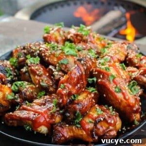 a large plate piled with huli huli chicken wings and garnished with sesame seeds, sriracha, and cilantro