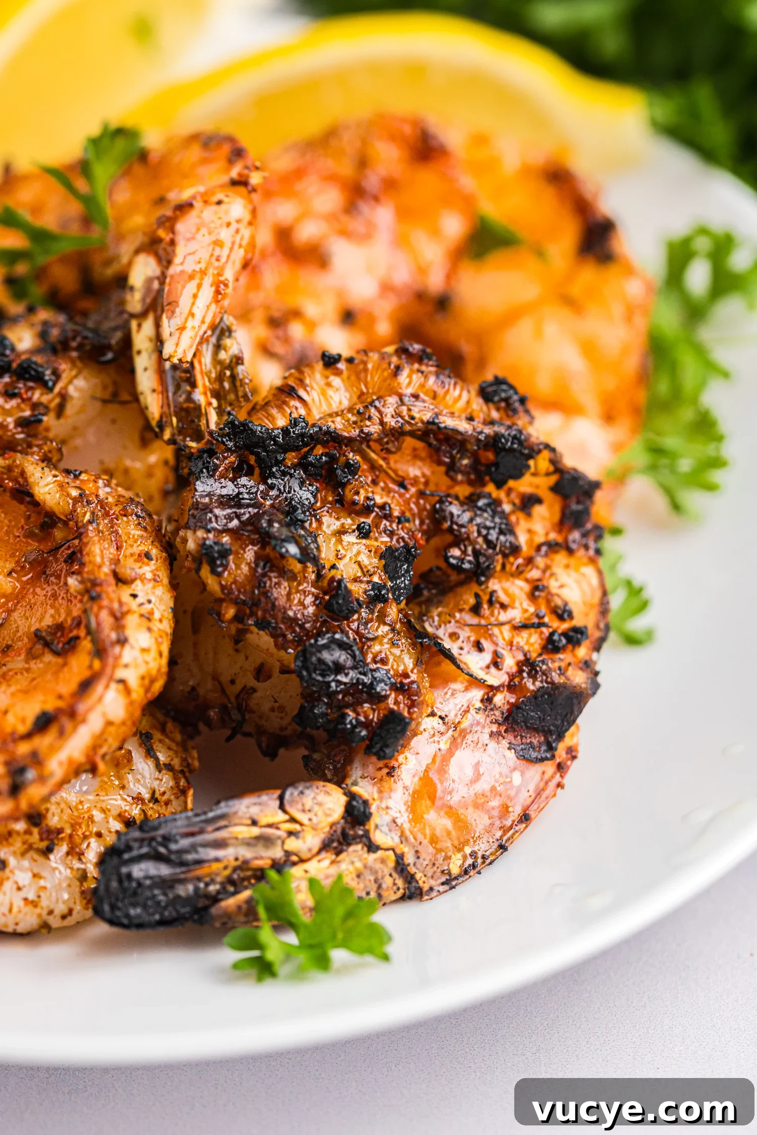 Juicy Cajun grilled shrimp with charred edges arranged on a plate, garnished with fresh parsley and lemon.
