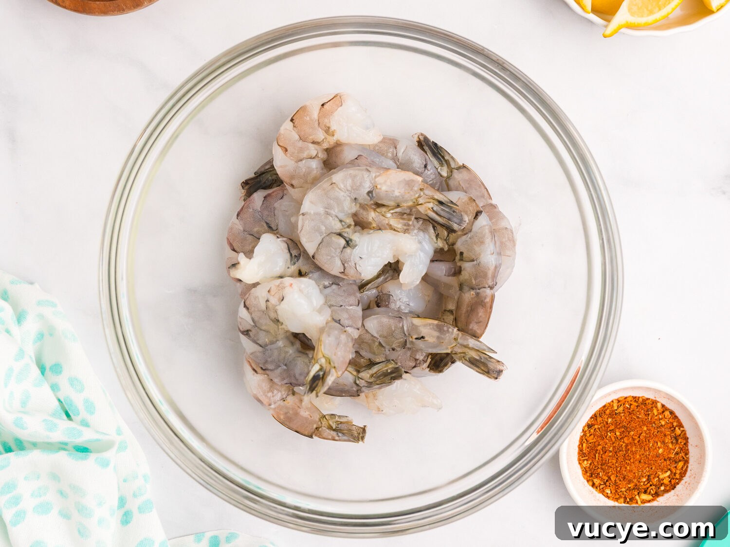 Raw shrimp placed in a clear glass bowl, ready for seasoning, with Cajun spice mix nearby.
