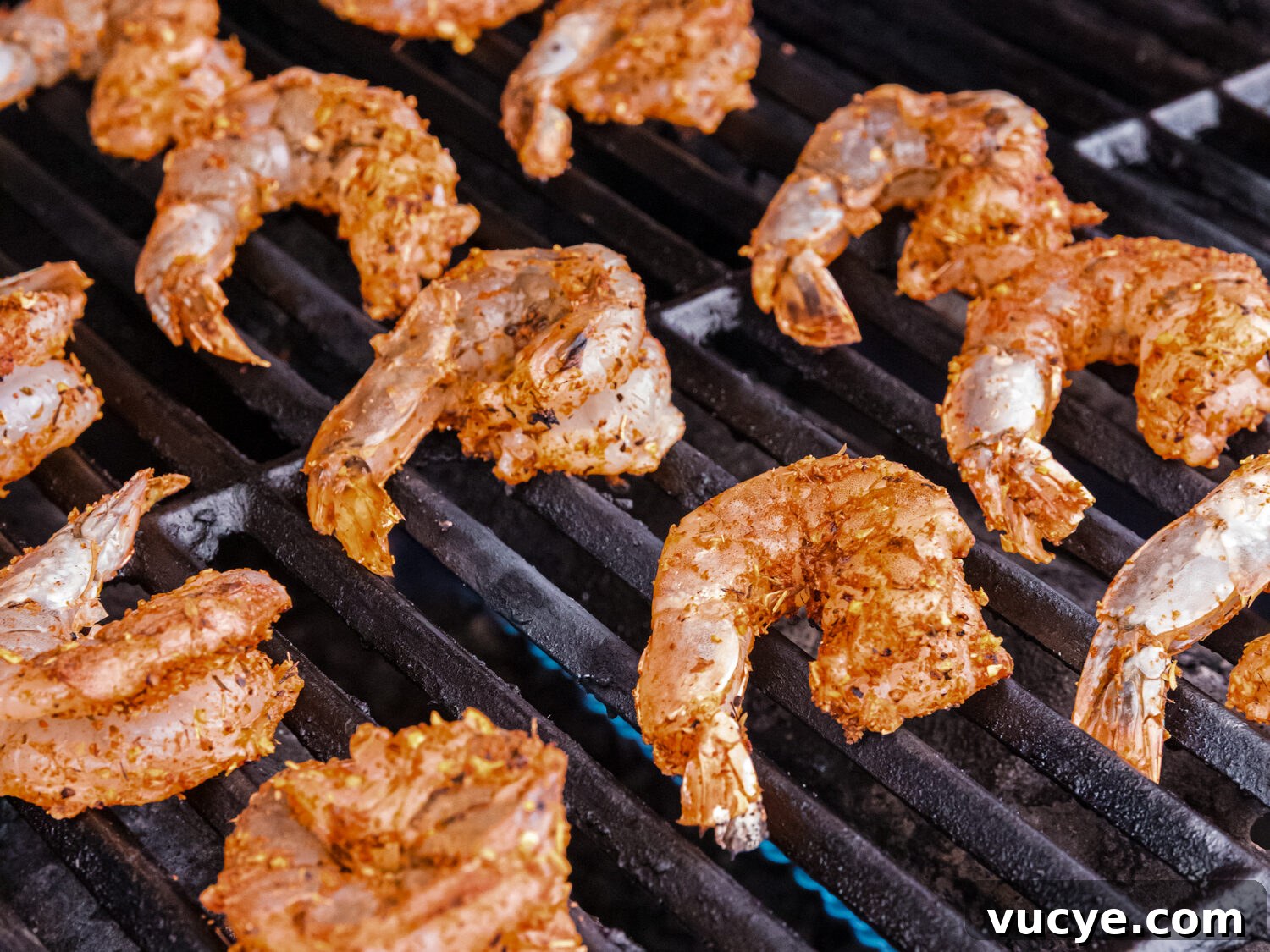 Seasoned shrimp placed directly on a grill with flames underneath, beginning to cook.
