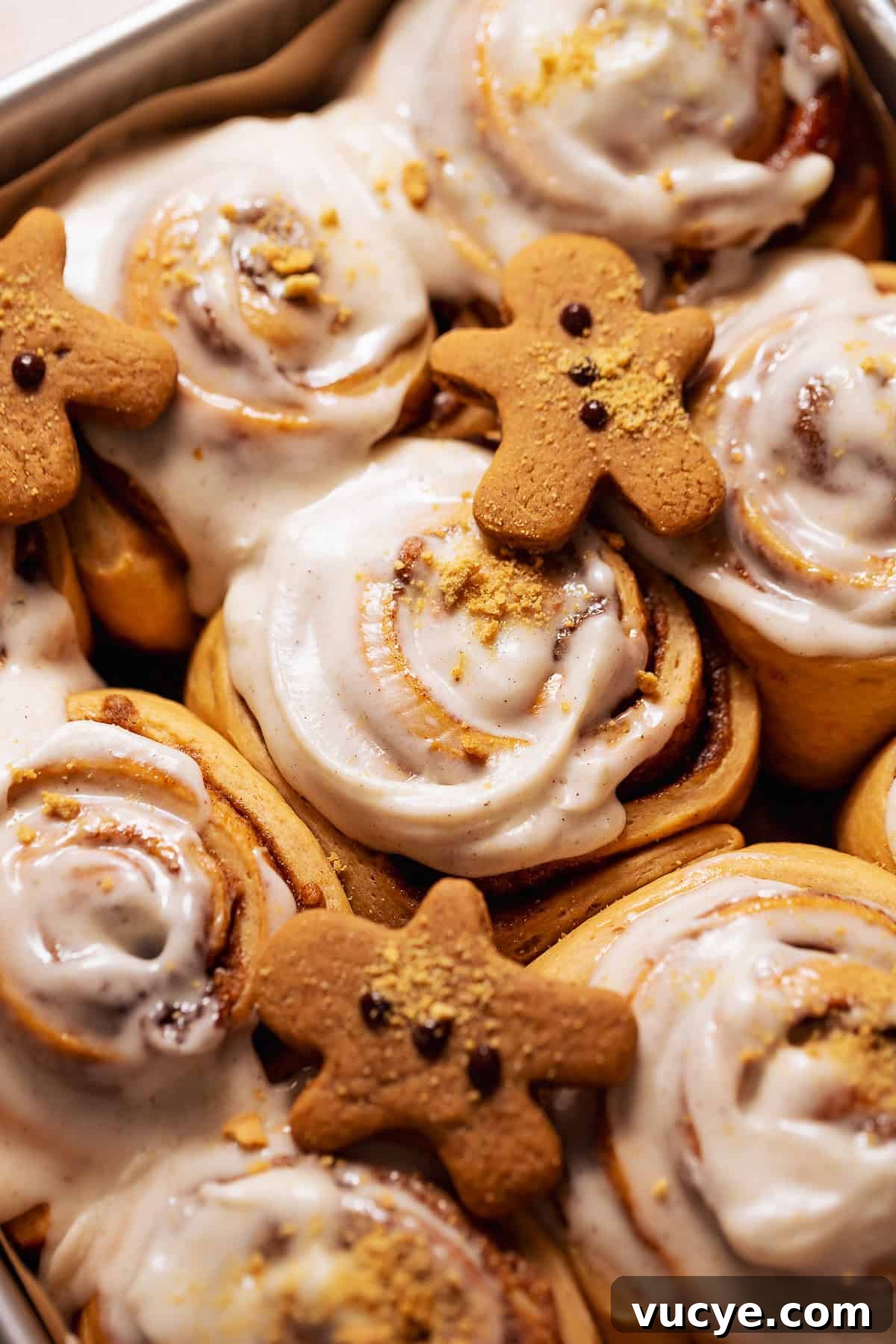Ultra-Soft Gingerbread Cinnamon Rolls with Molasses Swirl 2 Gingerbread rolls with mini gingerbread cookies on top in a baking pan.