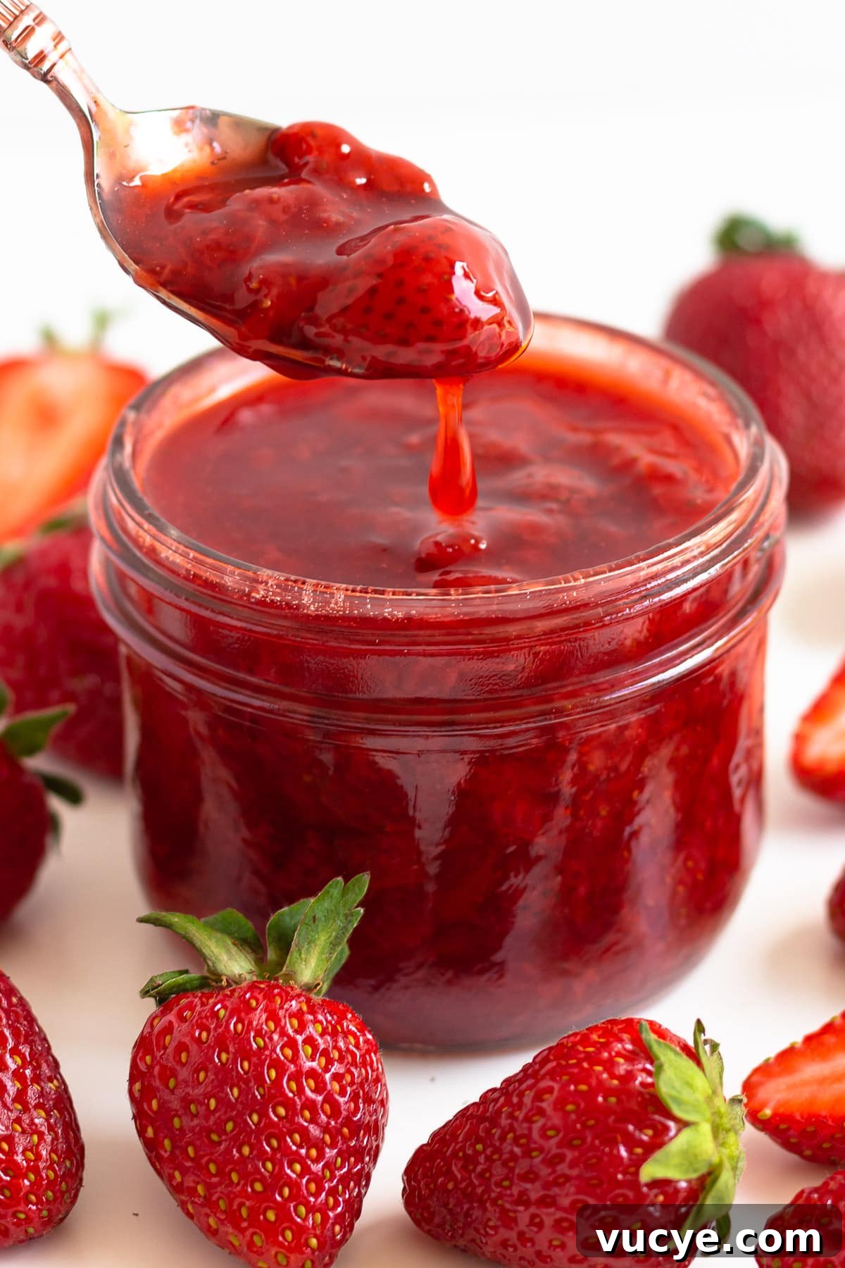 Must-Try Strawberry Recipes for Every Season 4 Strawberry compote dripping off a spoon into a jar surrounded by fresh strawberries.