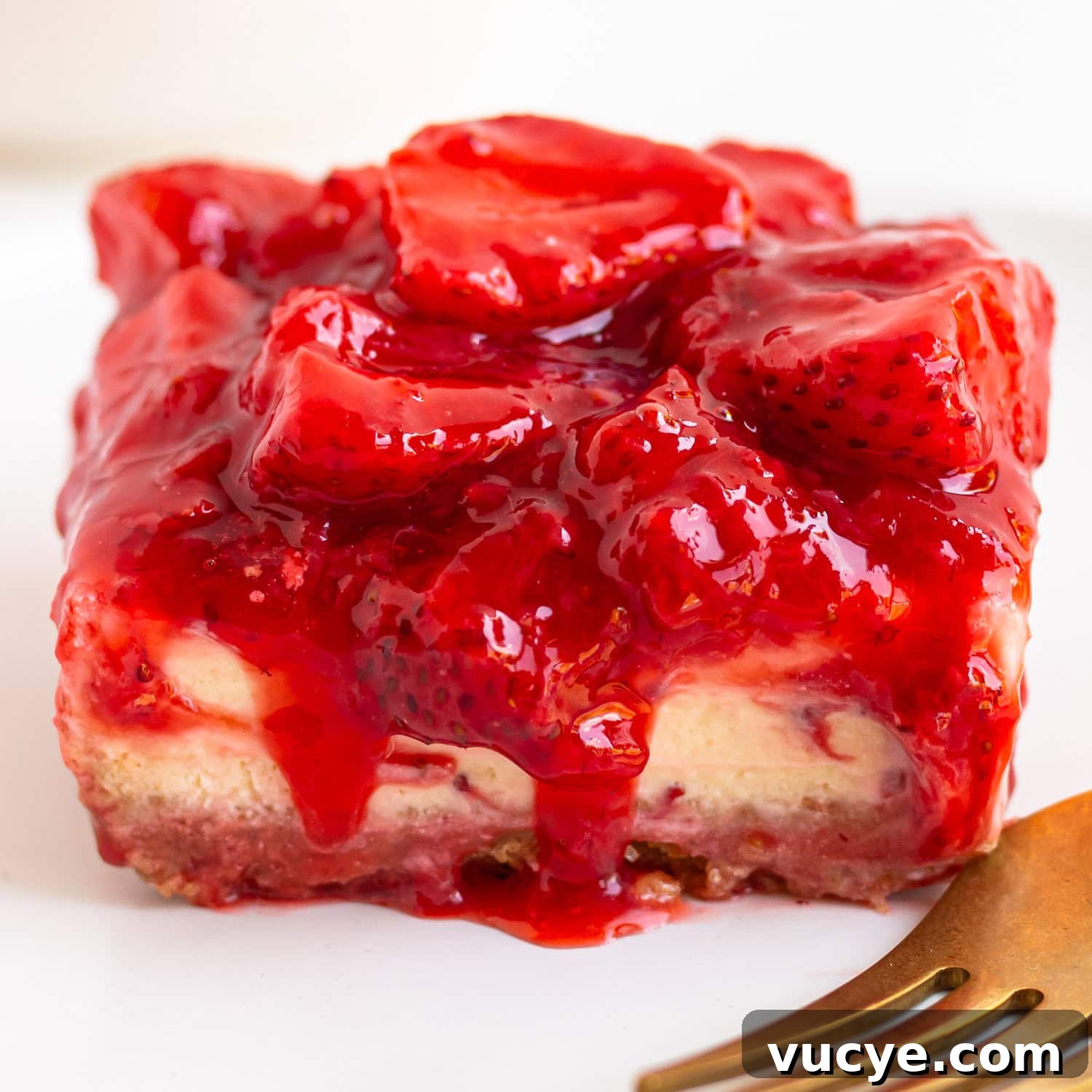 Must-Try Strawberry Recipes for Every Season 6 Closeup of a strawberry cheesecake bar with a gold colored fork in the corner.