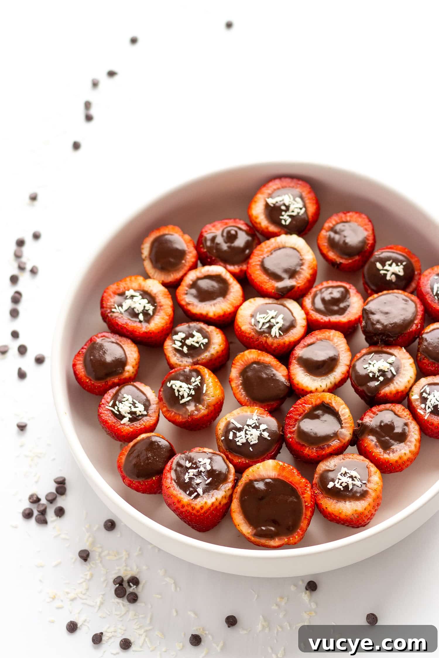 Must-Try Strawberry Recipes for Every Season 7 White bowl filled with chocolate coconut cream stuffed strawberries with chocolate chips and shredded coconut scattered beside the bowl.