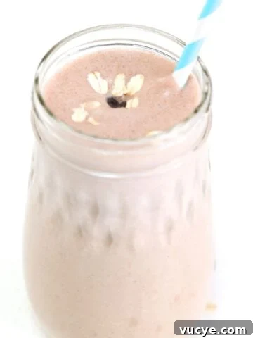 One Peanut Butter Banana Oatmeal Smoothie in a glass jar topped with oats and a mini chocolate chip, served with a straw.