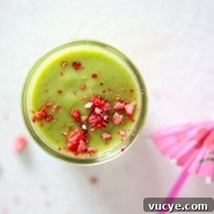 Top view of a green smoothie in a glass mason jar topped with crushed dried strawberry pieces.