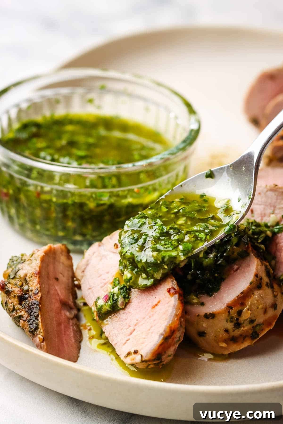 Grilled Pork Tenderloin with Chimichurri Sauce 2 Spooning chimichurri over a plate of sliced pork tenderloin.