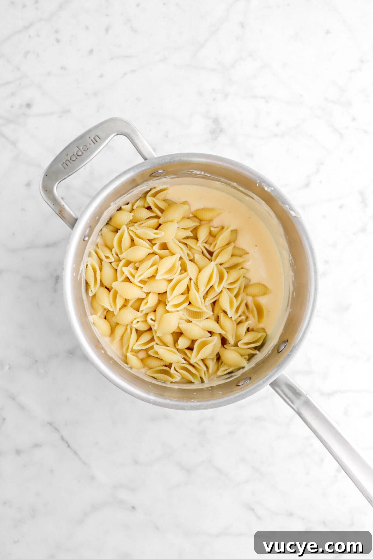 Creamy Four-Cheese Macaroni and Cheese Recipe 15 macaroni shells and cheese sauce in small pot on marble surface