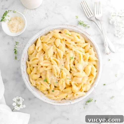 Creamy Four-Cheese Macaroni and Cheese Recipe 18 bowl of mac and cheese on marble surface with two forks, thyme sprigs, bowl of cheese, and white flowers around