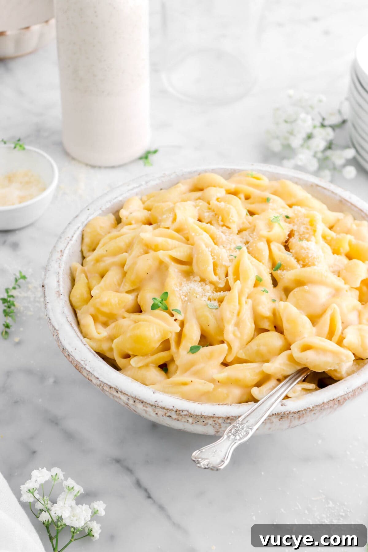 Creamy Four-Cheese Macaroni and Cheese Recipe 6 angled close up of mac and cheese with fork in bowl, flowers and base behind