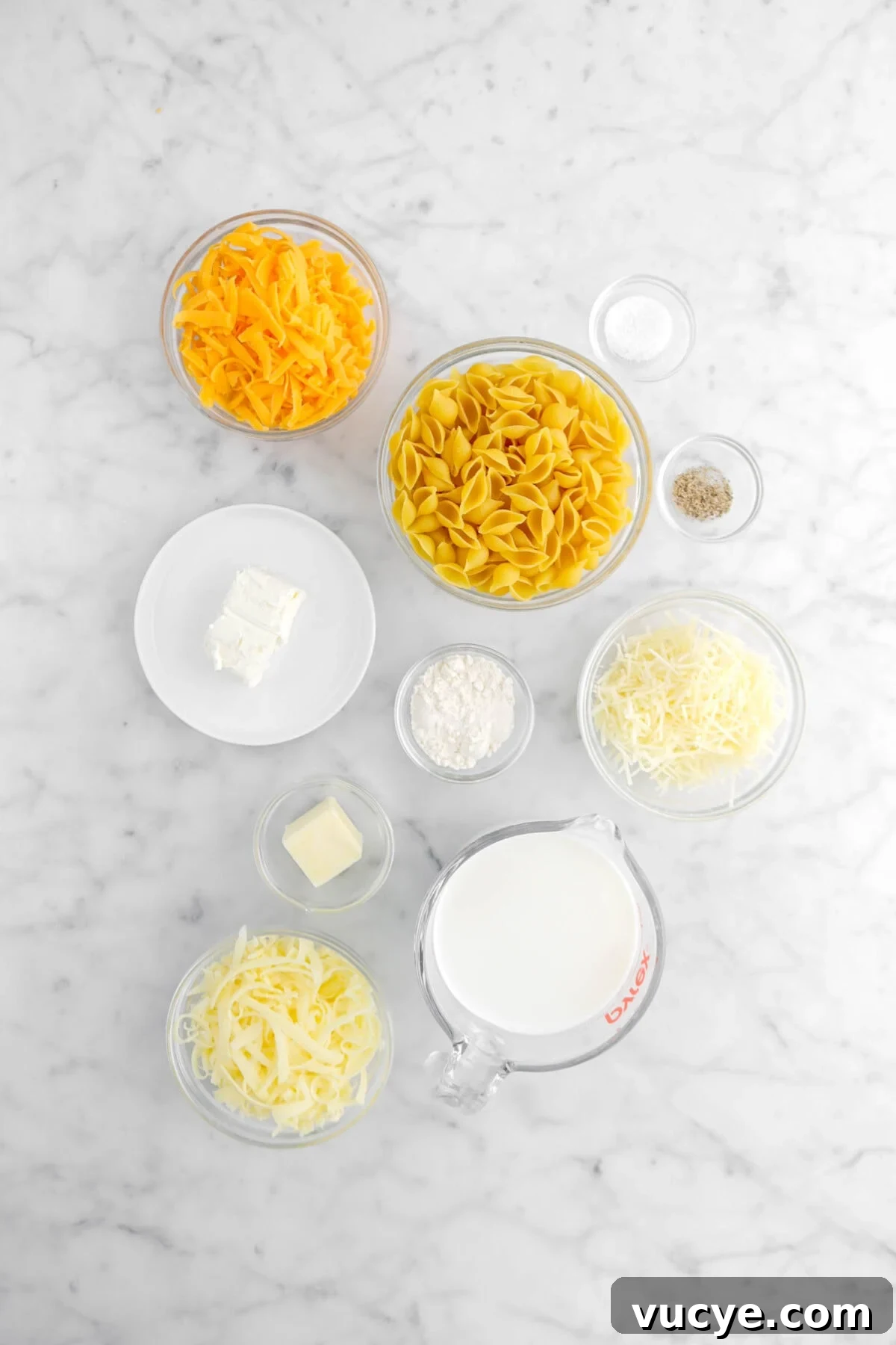 Creamy Four-Cheese Macaroni and Cheese Recipe 7 cheddar cheese, macaroni shells, salt, pepper, cream cheese, flour, parmesan, butter, milk, and white cheddar on marble surface