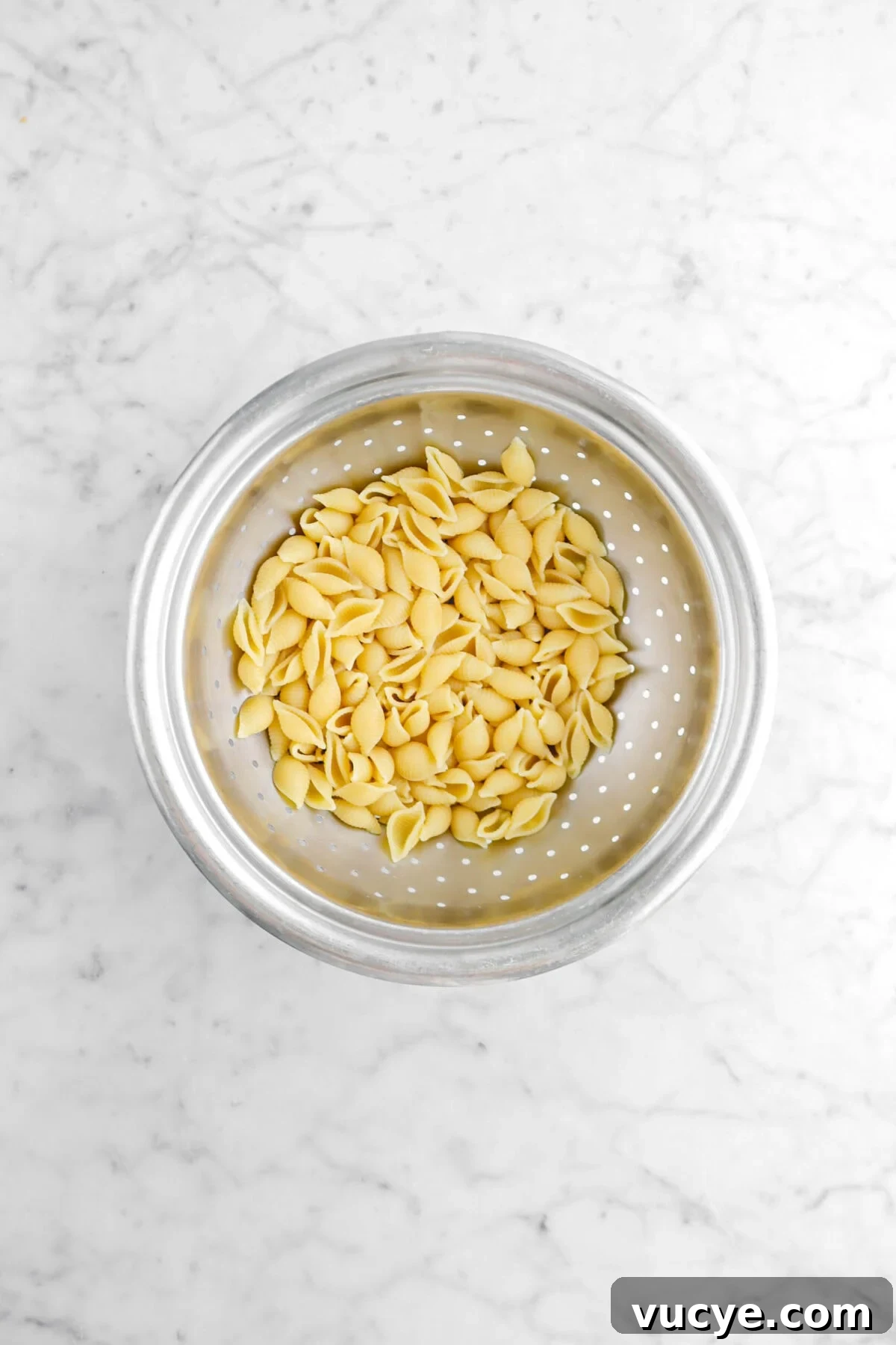 Creamy Four-Cheese Macaroni and Cheese Recipe 8 cooked medium macaroni shells in colander on marble surface