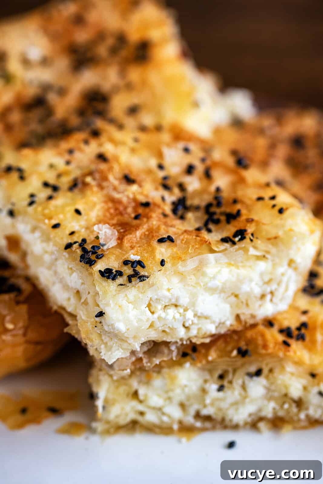 Tiropita: Authentic Greek Cheese Pie Recipe You Can Make at Home 3 Close-up of flaky, golden-brown Tiropita, with crisp phyllo pastry filled with white cheese and topped with black sesame seeds, stacked on a white surface.