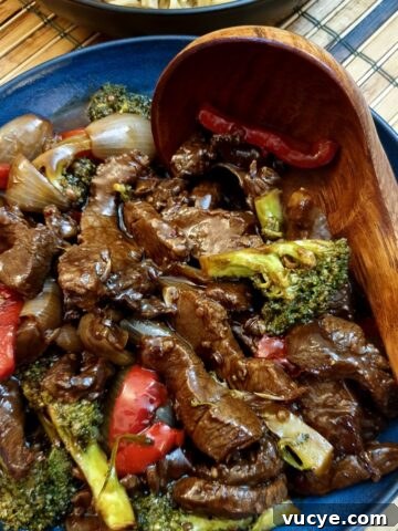 A blue dish filled with Szechuan beef stir fry with a wooden serving spoon.